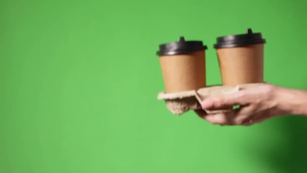 Deux café offre spéciale ou promo. Mains tenant deux tasses sur fond vert. Thé ou café à emporter. Tasse en papier brun avec couvercle noir. - Séquence, vidéo