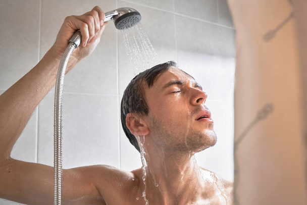 Portret młodego przystojniaka myje się żelem pod prysznic, mieli głowę szamponem w łazience w domu zbliżenie - Zdjęcie, obraz