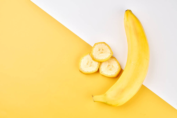 Banana creative background. Yellow and white backdrop with whole, peeled, sliced bananas - Foto, Imagen