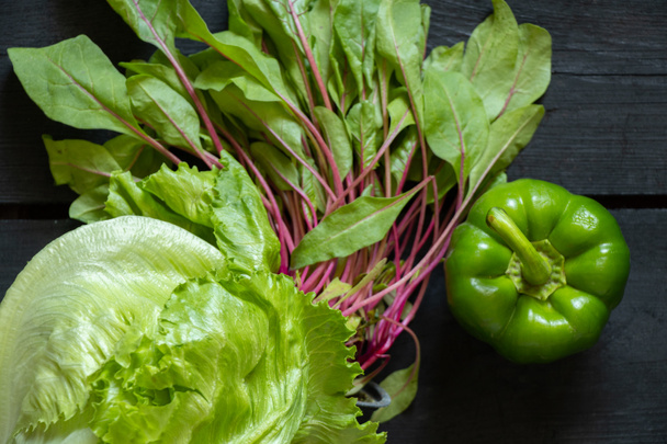 hojas de lechuga de col iceberg acelga suiza y pimientos verdes dulces en una mesa negra de madera, verduras para ensalada, verduras crudas - Foto, imagen