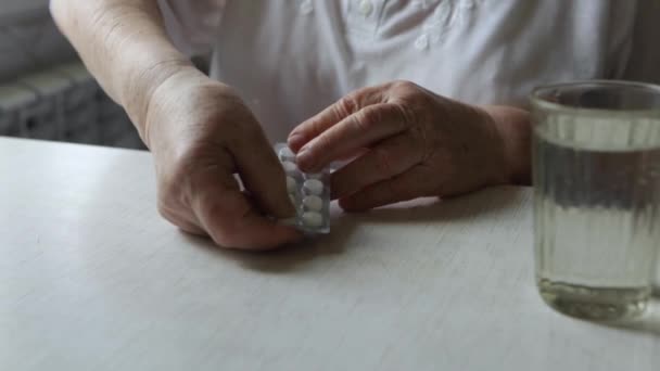 Sad old woman taking pills, health problems in old age, expensive medications. An elderly woman's hands unpacking several pills for taking medication. Grandma takes tablet and drinks a glass of water - Footage, Video