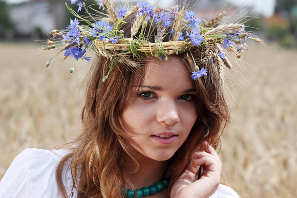 Beautiful young girl in summer field with grain and flower garland - Foto, Imagen