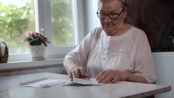 Eine ältere Frau, die zu Hause am Tisch in der Küche sitzt, hält Hausrechnungen, hat das Gefühl, sie habe vergessen zu zahlen oder Schulden zu machen. Rentnerin mittleren Alters - Filmmaterial, Video