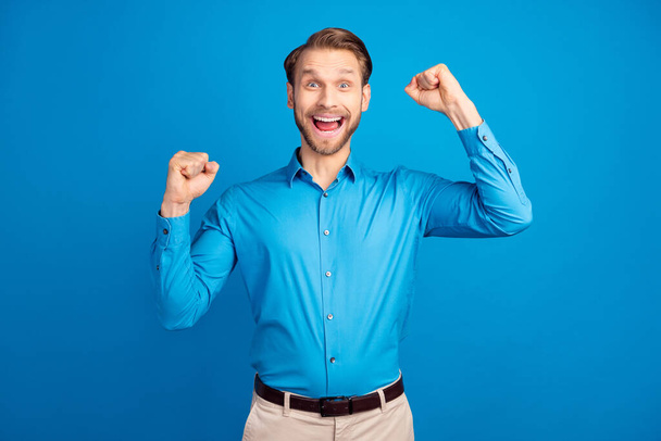 Photo of young man happy positive smile rejoice victory ecstatic achievement fists hands isolated over blue color background - Zdjęcie, obraz