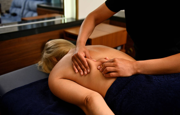Woman lying on massage table and relaxing being massaged by masseur in spa resort center. Sports massage, Physical treatment of the body - Φωτογραφία, εικόνα