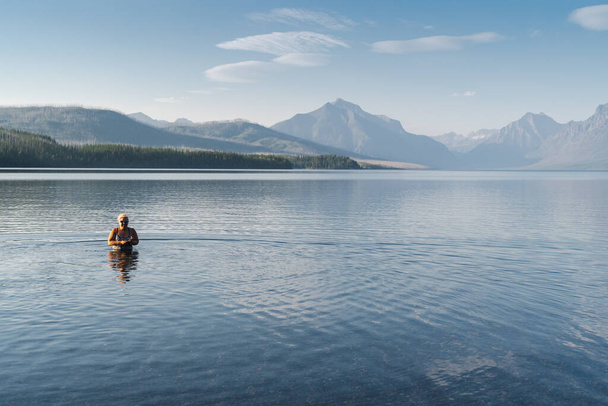 Blonde adult woman enjoys taking a dip in the cold waters of Lake McDonald in Glacier National Park during a heatwave - Photo, Image