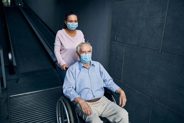 Pensionné et dame aidante descendant l'escalier mobile - Photo, image