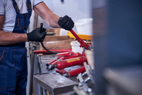 Male worker assembling portable hydraulic car repairing tool in garage - Foto, immagini