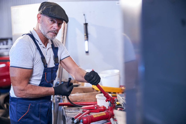 Bearded male worker assembling portable hydraulic jack in garage - Photo, Image