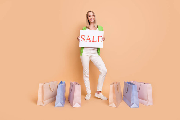 Full length body size photo woman near bags after shopping keeping sale table isolated pastel beige color background copyspace - Фото, изображение