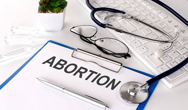 ABORTION text on white paper on the white background. stethoscope ,glasses and keyboard - Foto, imagen