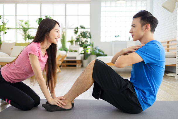 Young woman helping young man to do crunches at home . - Photo, Image