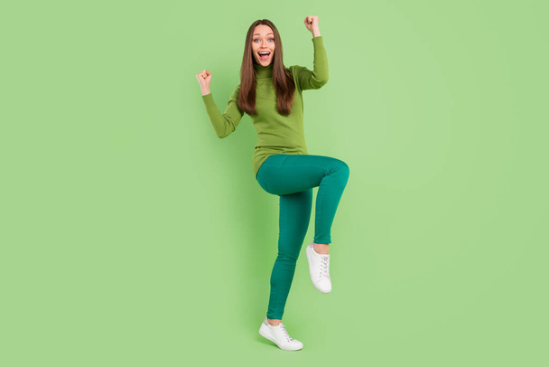 Full body photo of attractive young nice lady good mood raise fists winner isolated on green color background - Фото, зображення