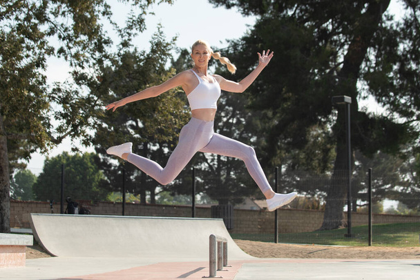 Здоровая и здоровая блондинка, прыгающая вправо через препятствия в парке, глядя вперед. - Фото, изображение