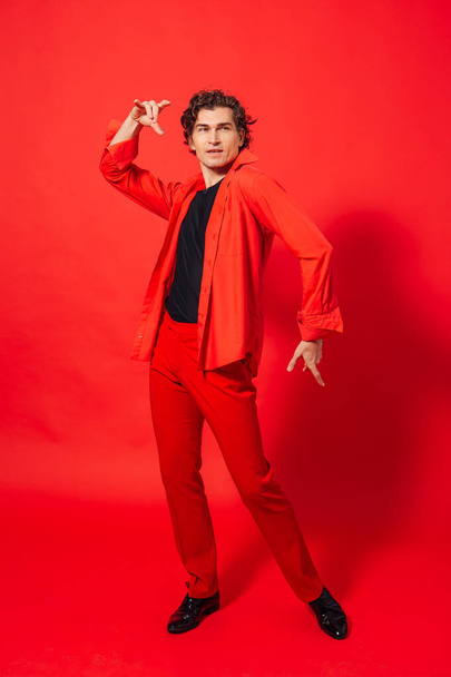 Portrait of a tall handsome man dressed in red shirt posing on the red background. - Φωτογραφία, εικόνα