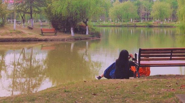 Молодая женщина сидит на скамейке и читает книгу на озере - Фото, изображение