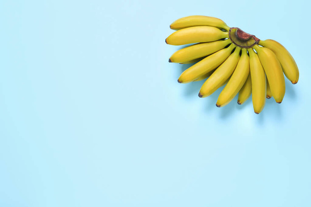 Bunch of ripe baby bananas on light blue background, top view. Space for text - Fotó, kép