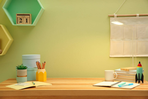 Stylish workplace with stationery on wooden desk near light green wall. Interior design - Photo, Image