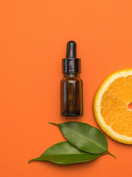 A bottle with an eyedropper, a piece of orange and leaves on an orange background. The concept of therapy with natural remedies. - Fotografie, Obrázek