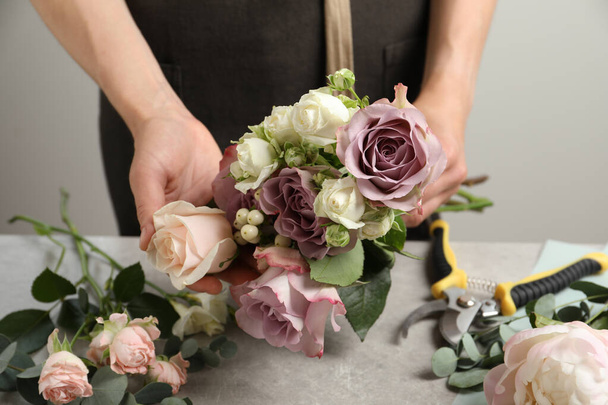 Florist creating beautiful bouquet at grey table against light background, closeup - Foto, afbeelding