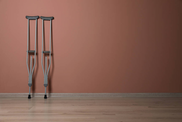 Pair of axillary crutches near pale pink wall. Space for text - Foto, immagini