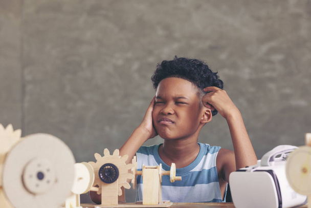 Niño negro africano pensando contemplando el diseño y mirando hacia arriba y teniendo el mecanismo de simulación modelo robot de madera en la mesa en el aula. - Foto, Imagen