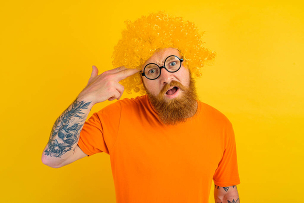 hombre con barba, peluca amarilla y gafas hace un gesto de arma con la mano - Foto, Imagen