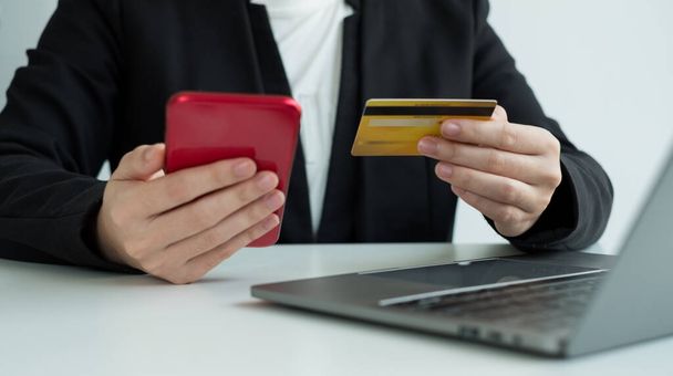 Firma trzyma w ręku kartę kredytową i używa smartfona do zakupów internetowych i płatności internetowych w biurze. - Zdjęcie, obraz