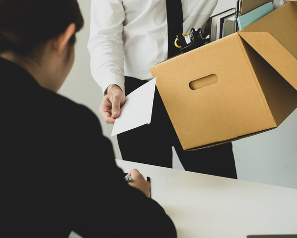 Отчаянно уволенный офисный работник вручает работодателю заявление об увольнении и упаковывает свои вещи в картонную коробку с концепцией увольнения и безработицы. - Фото, изображение