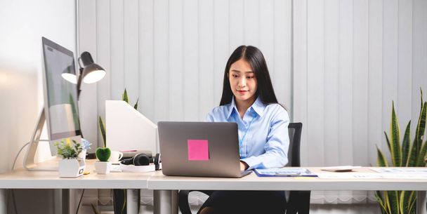 Asiatin arbeitet im Büro an einem Laptop mit einem fröhlichen und glücklichen Lächeln. - Foto, Bild