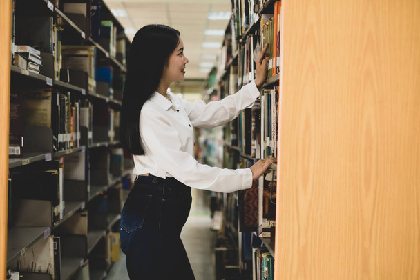 Giovani donne asiatiche sono alla ricerca di libri e libri di lettura sulle tabelle e navate delle biblioteche universitarie per la ricerca e lo sviluppo del loro sé accademico ed educativo. - Foto, immagini
