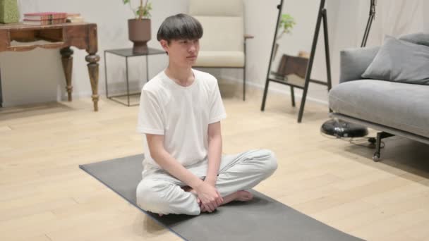 Азиатский мужчина медитирует на коврике для йоги дома - Кадры, видео