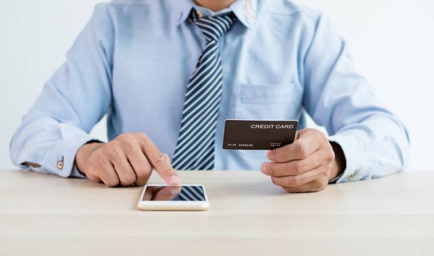 İş adamının elinde bir kredi kartı var ve internet üzerinden alışveriş ve internet üzerinden ödeme yapmak için akıllı telefon kullanıyor.. - Fotoğraf, Görsel