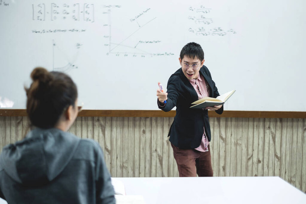 Un enseignant asiatique dans une salle de classe près du tableau blanc écrit et enseigne une leçon avec une conférence spéciale dans une colonne de classe. Un professeur de mathématiques explique les sommes arithmétiques aux étudiants universitaires. - Photo, image