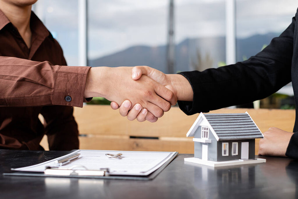 Biznesmeni i maklerzy agenci nieruchomości uścisną sobie dłonie po zakończeniu negocjacji w sprawie ubezpieczenia domów i podpisania umów. Koncepcja ubezpieczenia domowego. - Zdjęcie, obraz
