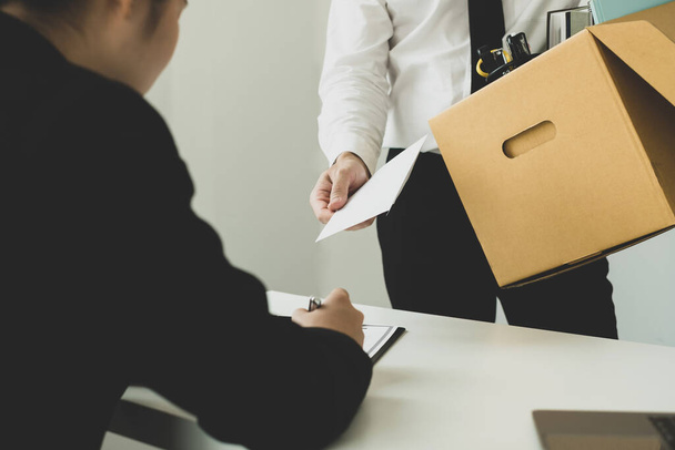 Desperately fired man office worker employee hands her employer her resignation letter and packs her belongings in a cardboard box concept dismissal and unemployment. - Photo, Image