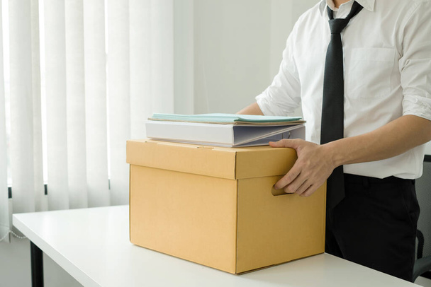 A man office worker is unhappy with being fired from a company packing things into cardboard boxes. The young man was stressed and disappointed by being fired. concept of layoffs and unemployment. - Foto, Imagem