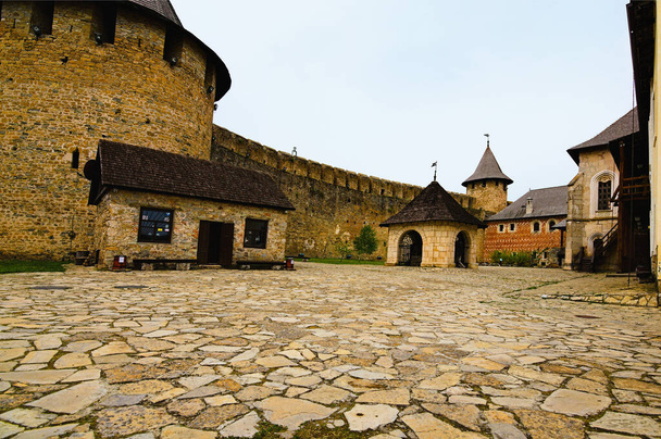 Wide-angle landscape view of courtyard with ancient stone buildings in the old medieval castle. High stone wall with tower in the background. Famous touristic place and romantic travel destination. - Photo, Image