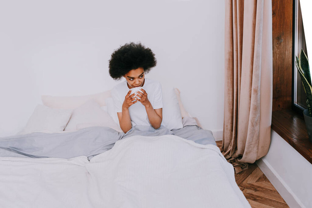 Afro-american girl resting in bed at home - Beautiful woman relaxing at home having breakfast in bed - Фото, зображення