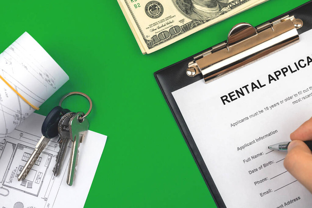 Man filling out rental application agreement. Clipboard with official application form. Table with money and house keys. Green background  - Photo, Image