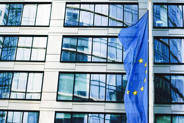 Флаг Европейского Союза, размахивающий перед зданием современного корпоративного офиса, символом Парламента, Комиссии и Совета ЕС - Фото, изображение