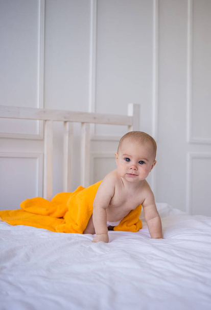 Pikkutyttö vaipassa ja oranssi pyyhe ryömii sängyllä. Lapsen kehitys - Valokuva, kuva