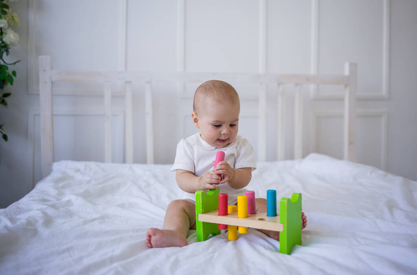bambina in un body bianco gioca con un giocattolo educativo sul letto - Foto, immagini