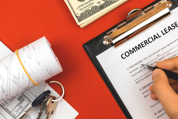 Man filling out commercial lease agreement. Clipboard with business document, house keys, pen and money. Red background, copy space  - Photo, Image