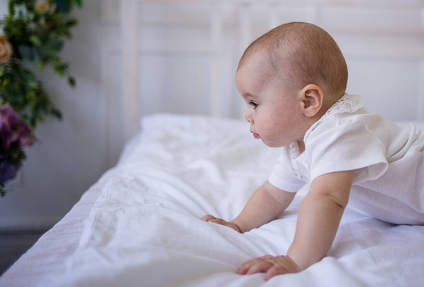 Porträt eines kleinen Mädchens im weißen Body, das auf dem Bett kriecht - Foto, Bild