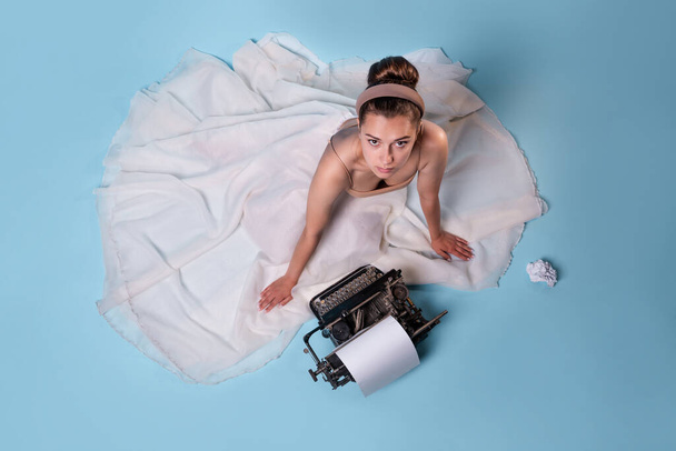 young romantic woman is an author at a typewriter, sitting on the floor in a fluffy white skirt - Foto, Imagem