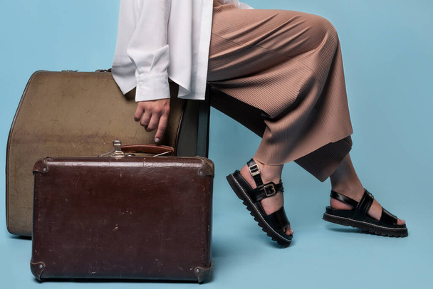 young woman in summer pants and a white shirt is sitting on vintage leather suitcases - Photo, Image