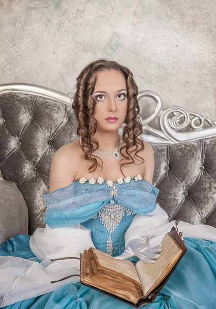 Kaunis nainen keskiaikaisessa mekossa kirjan kanssa sohvalla
 - Valokuva, kuva
