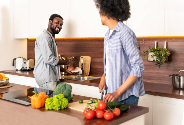 Beautiful afro american couple cooking at home - Beautiful and cheerful black couple preparing dinner together in the kitchen - Foto, immagini