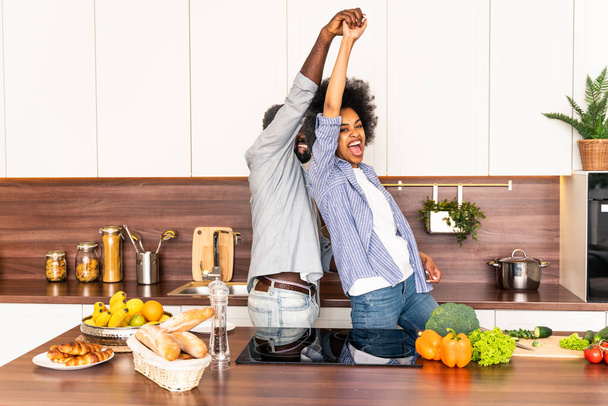 Beautiful afro american couple cooking at home - Beautiful and cheerful black couple preparing dinner together in the kitchen - Fotoğraf, Görsel
